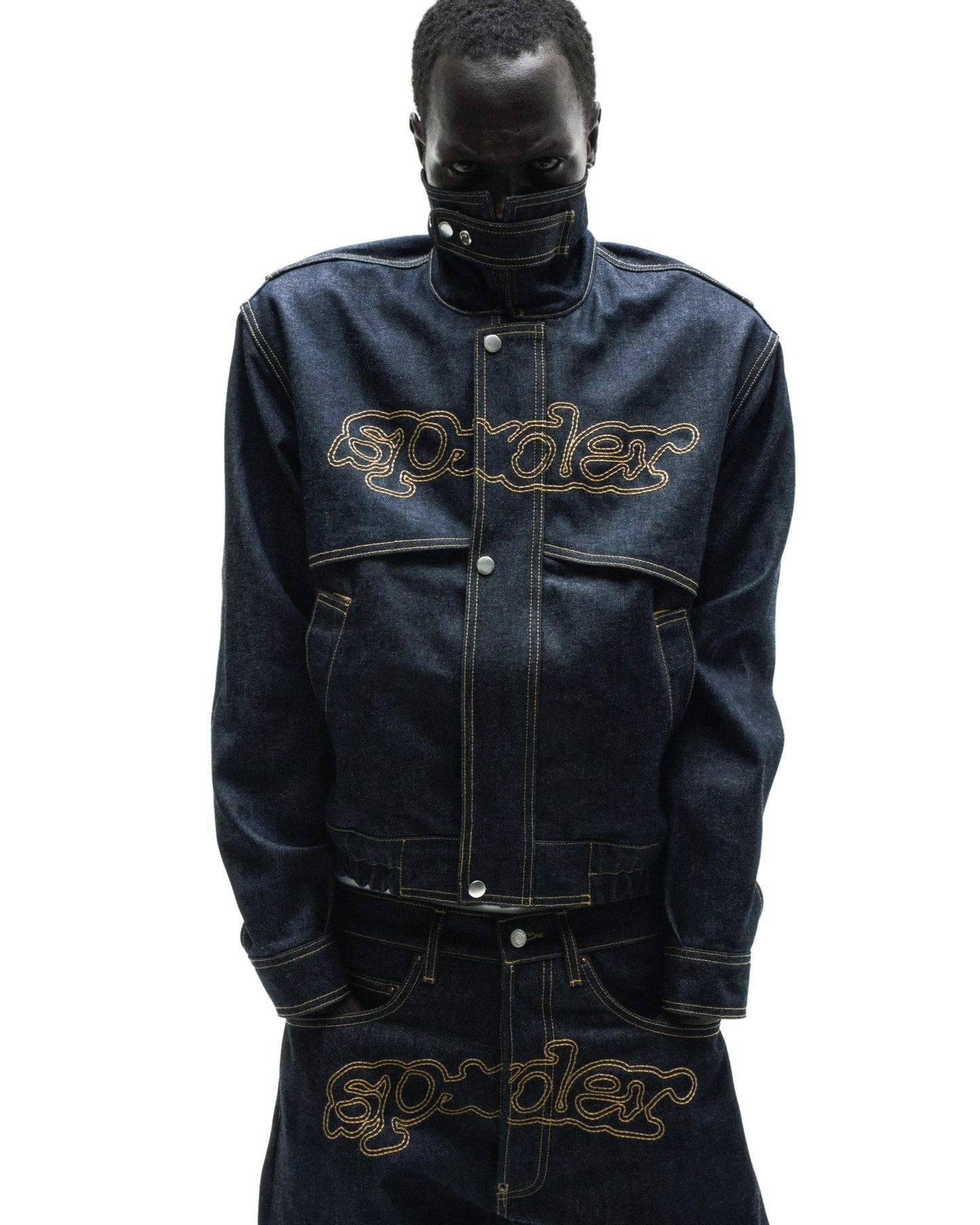 Dark wash denim jacket with yellow stitching, embroidered script logo, stand collar, and zipper placket.
