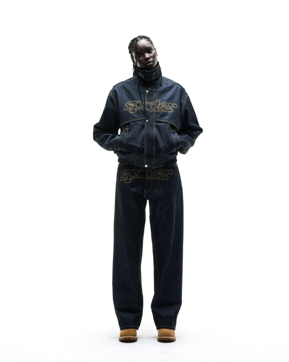 Dark wash denim jacket with yellow stitching, embroidered script logo, stand collar, zipper, and snap placket.