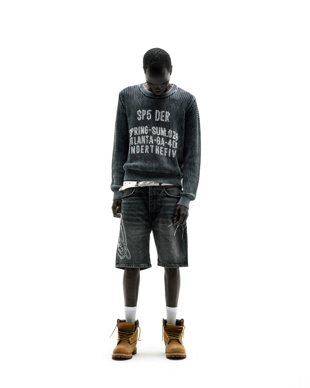 Black knit cotton UNDERTHEFIVE sweater with white text print, worn with dark denim shorts and tan boots.