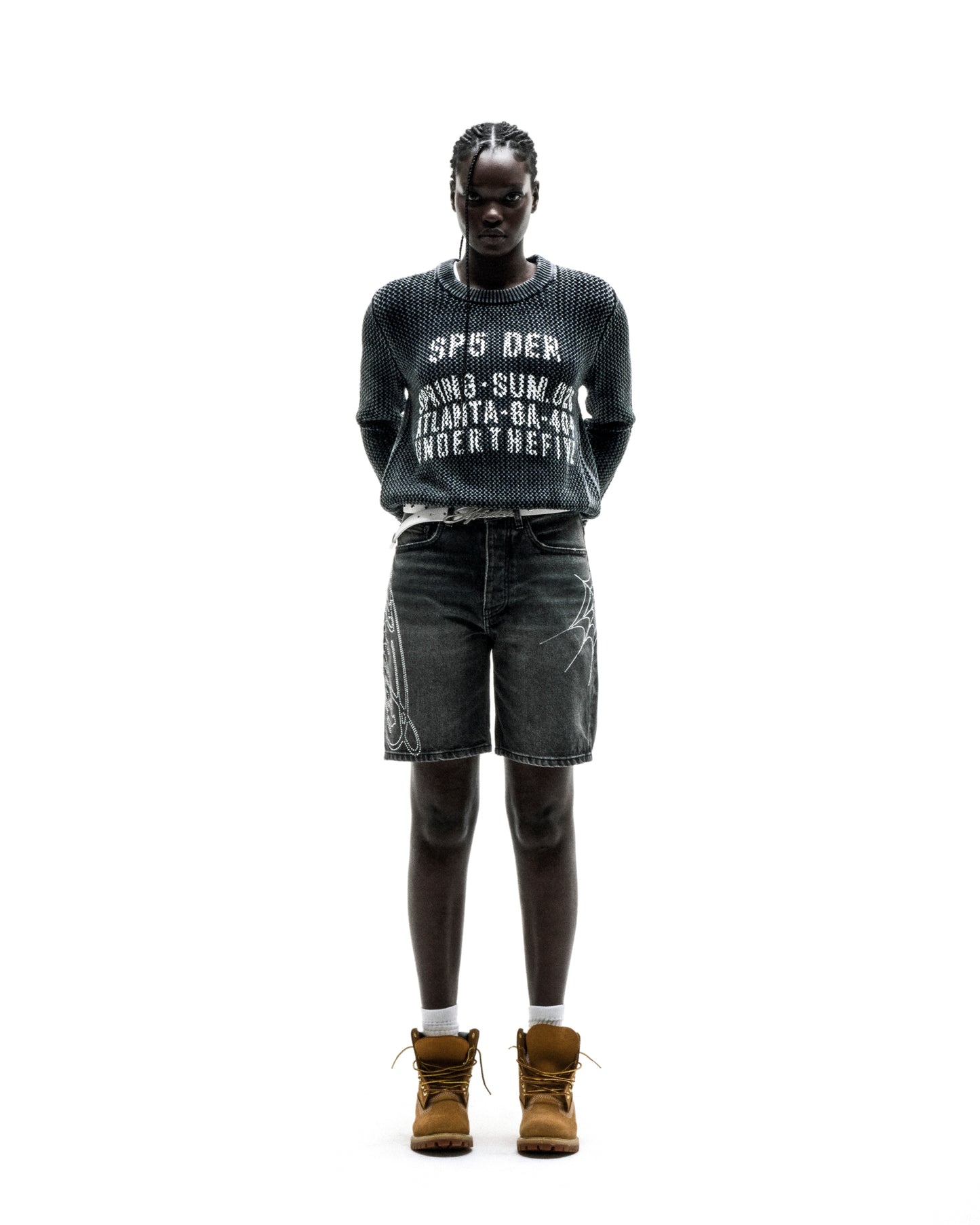 Black knit cotton UNDERTHEFIVE sweater with white text print, worn with dark denim shorts and brown boots.