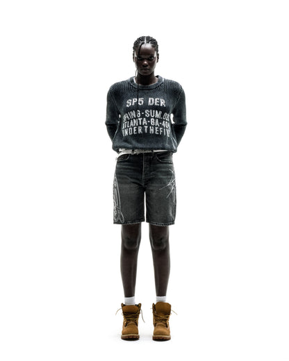 Black knit cotton UNDERTHEFIVE sweater with white text print, worn with dark denim shorts and brown boots.