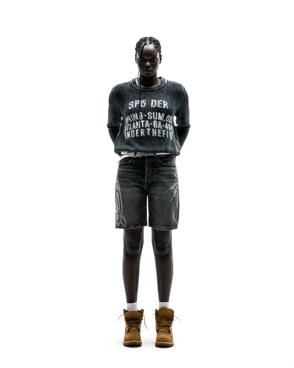 Black knit cotton UNDERTHEFIVE sweater with white text print, worn with dark denim shorts and brown boots.