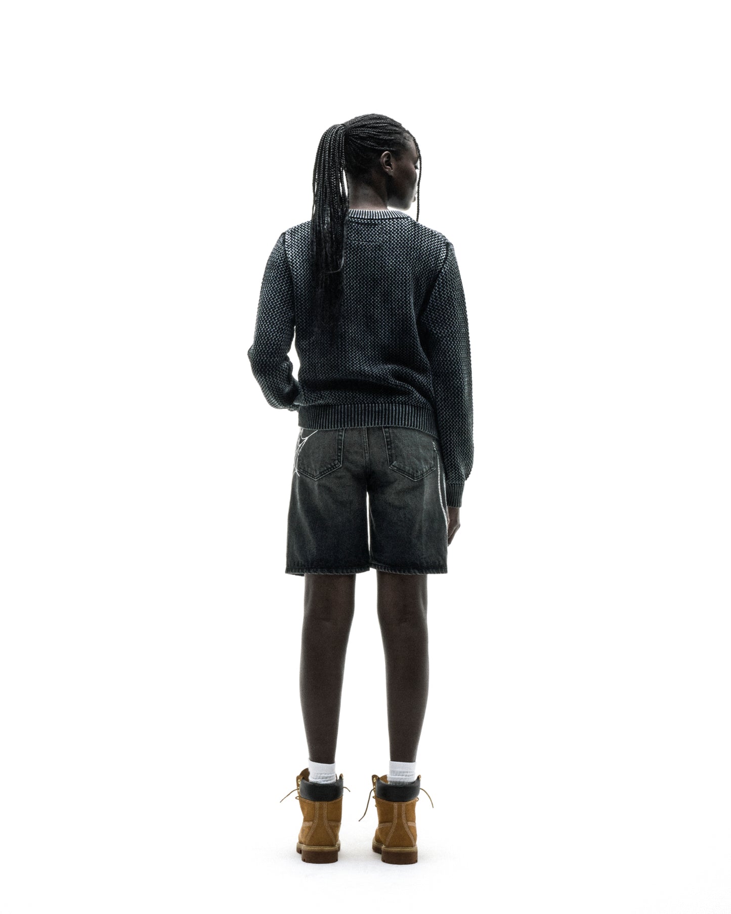 Person from behind wearing a dark knit cotton UNDERTHEFIVE sweater with text print, dark shorts, and brown boots.