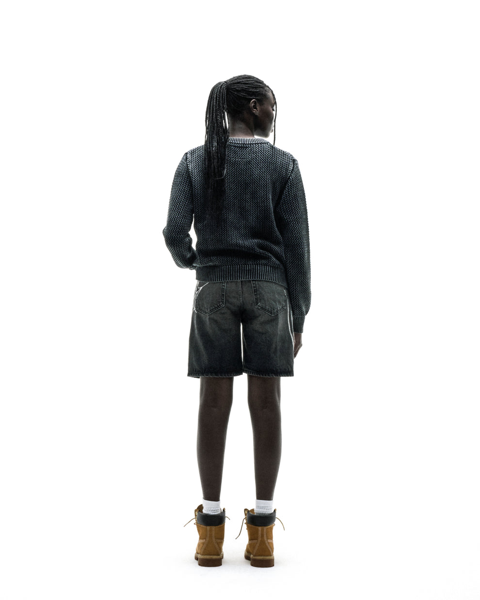 Person from behind wearing a dark knit cotton UNDERTHEFIVE sweater with text print, dark shorts, and brown boots.