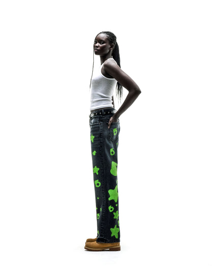 Model in faded wash denim pants with green Beluga stamp design, custom hardware, and straight leg fit.