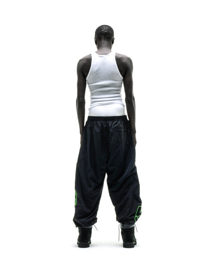 Black nylon track pants with green embroidered graphics, elastic cuffs, and paneled construction.