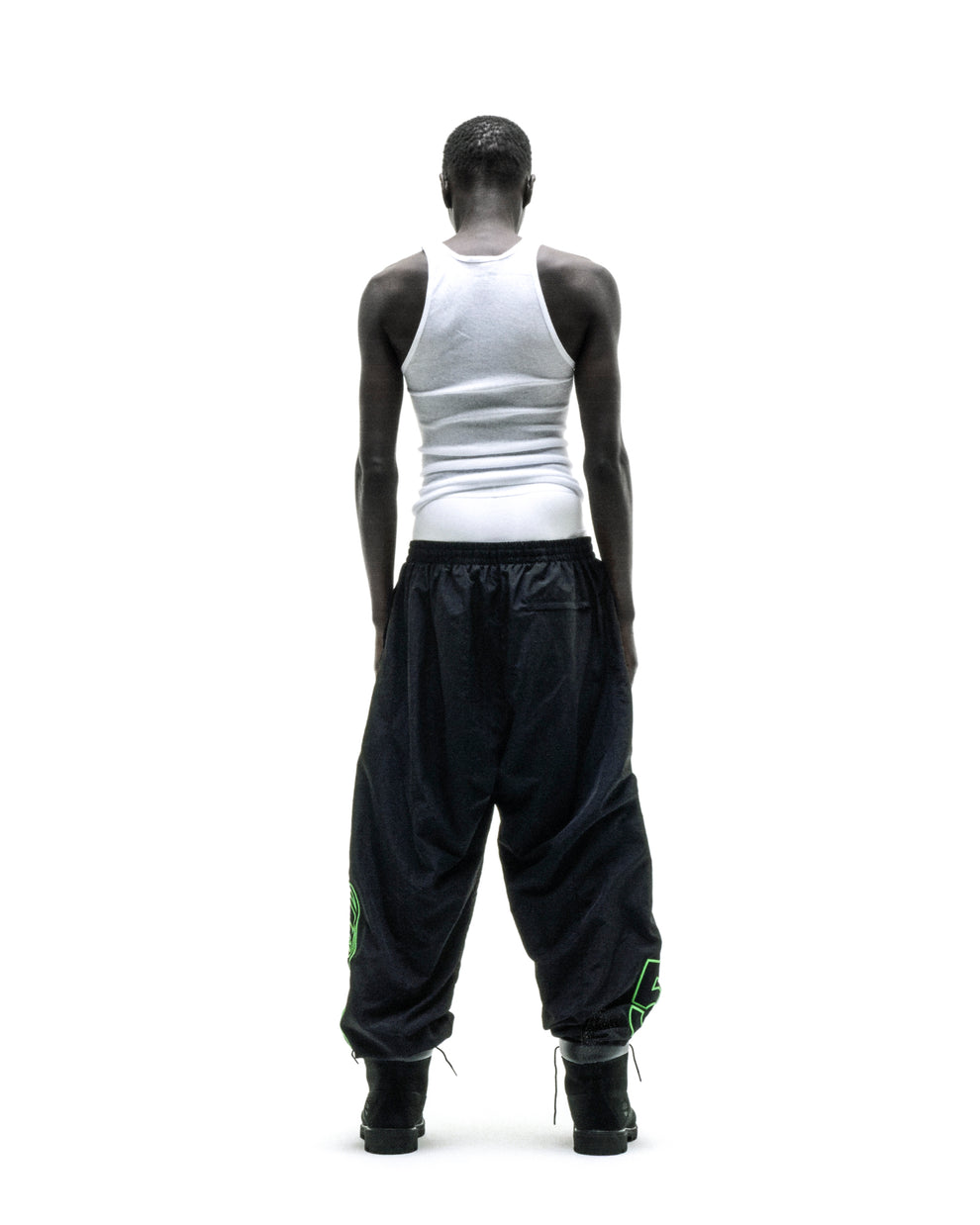 Black nylon track pants with green embroidered graphics, elastic cuffs, and paneled construction.