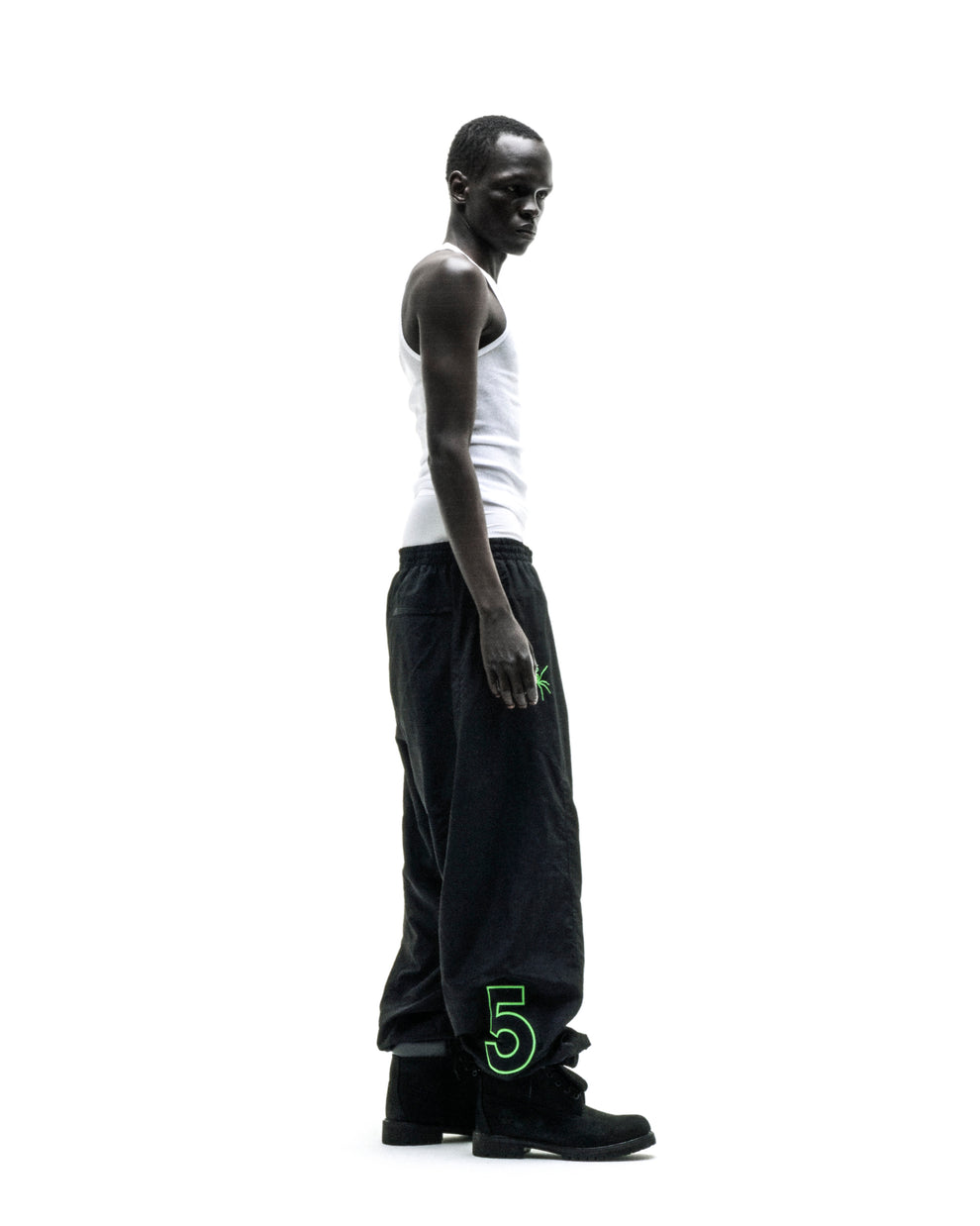 Black nylon SCRIPT WARM UP PANT with green embroidered graphic, worn by a man in a white tank top.