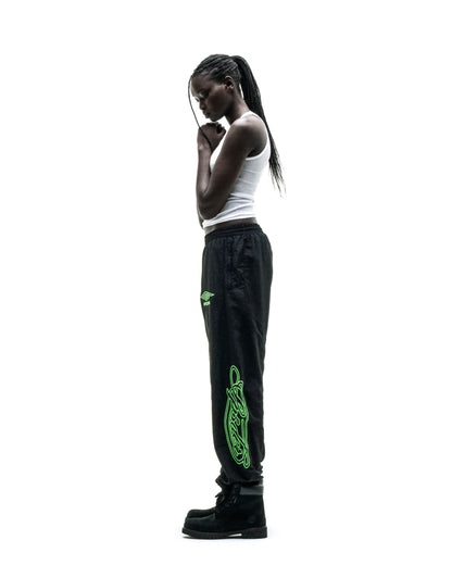 Black nylon track pants with green embroidered graphics and elastic cuffs.