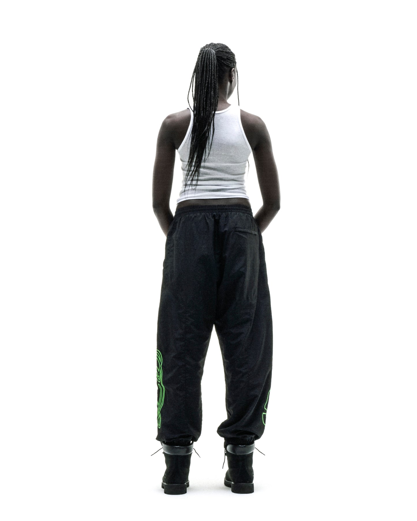 Black nylon track pants with green embroidered graphics, elastic cuffs, and paneled construction.