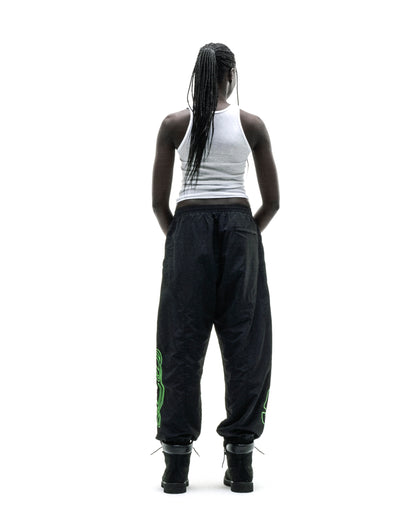 Black nylon track pants with green embroidered graphics, elastic cuffs, and paneled construction.