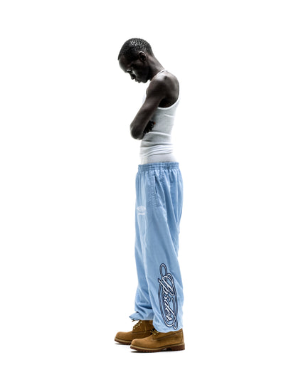 Light blue nylon SCRIPT WARM UP PANT with embroidered graphic, elastic cuffs, and paneled construction.