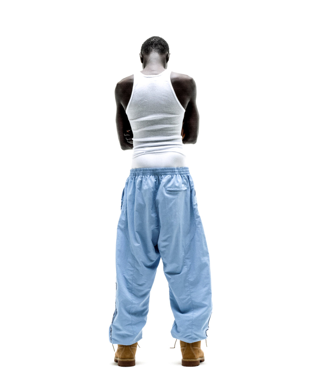 Back view of a person wearing light blue nylon SCRIPT WARM UP PANT with paneled construction and elastic cuffs.