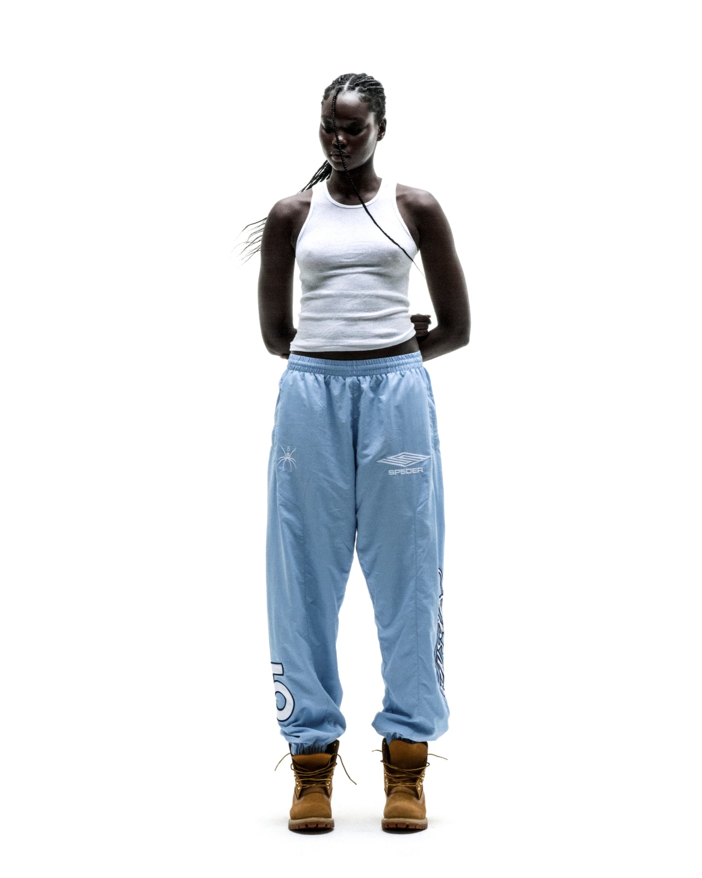 Woman in light blue nylon track pants with white embroidered graphics and elastic cuffs.