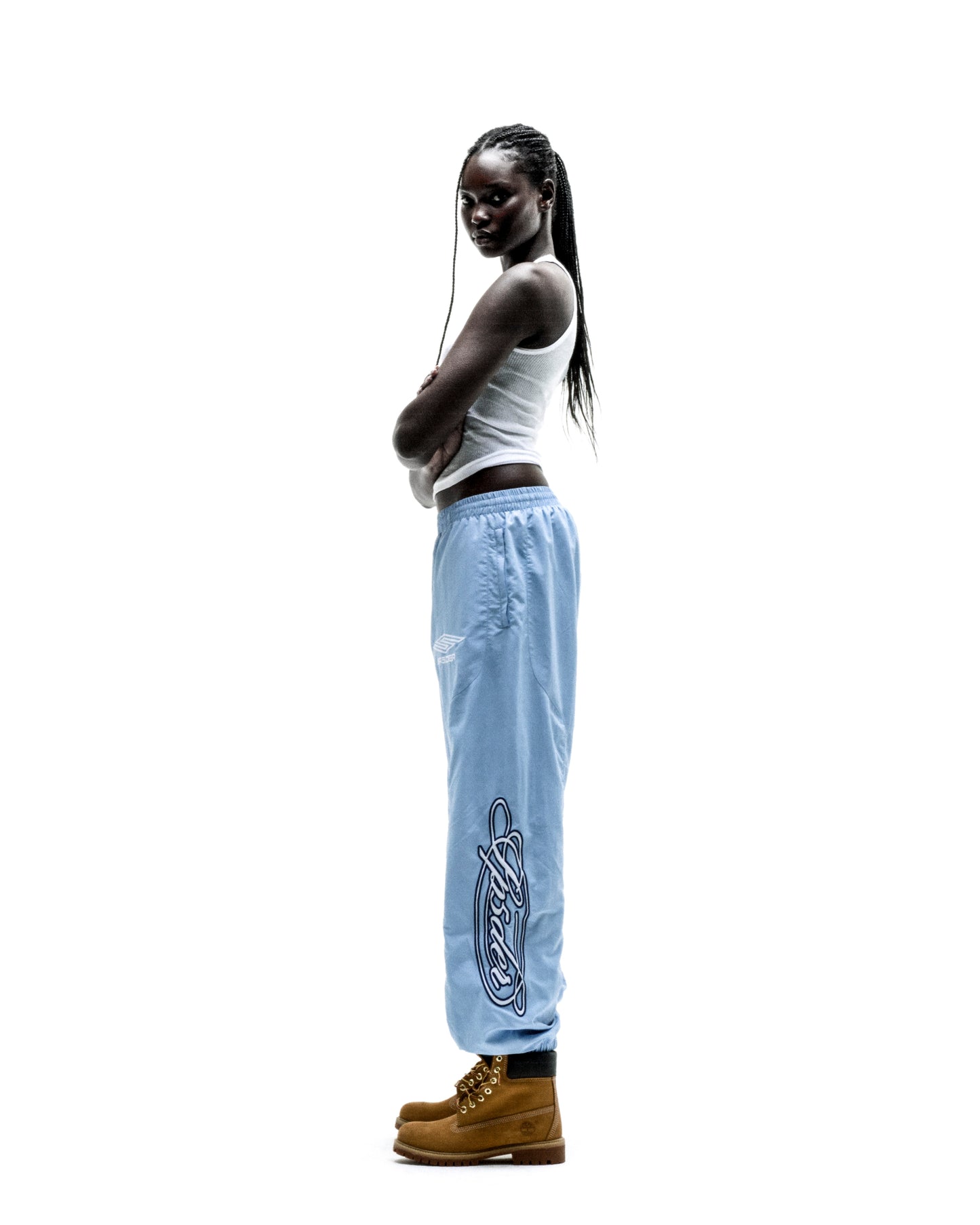 Light blue nylon track pant with embroidered script graphic, elastic cuffs, and paneled construction.