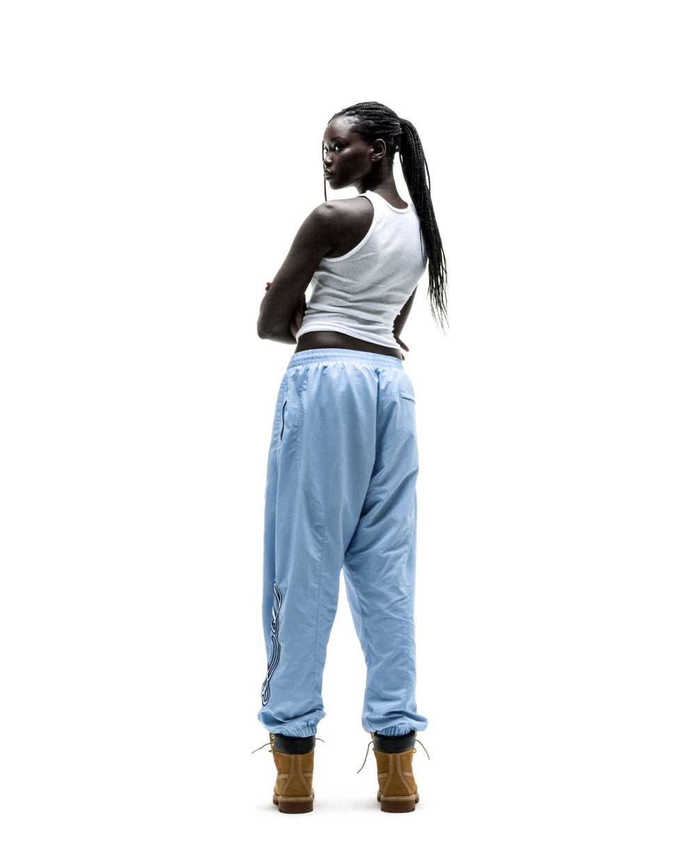 Woman in light blue nylon SCRIPT WARM UP PANT with embroidered graphics, elastic cuffs, and brown boots.