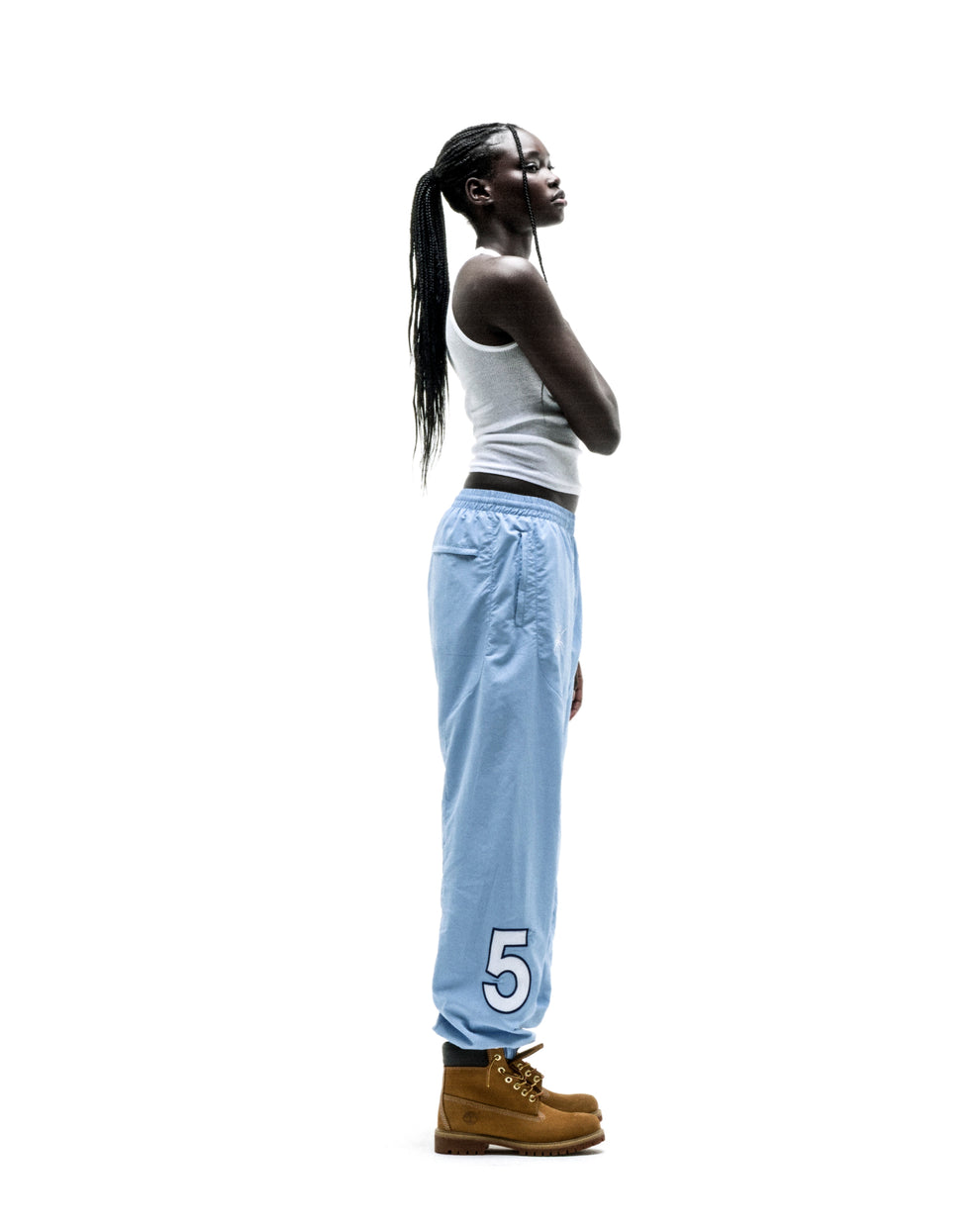 Woman in light blue nylon Script Warm Up Pant with large white "5" graphic, elastic cuffs, and brown boots.