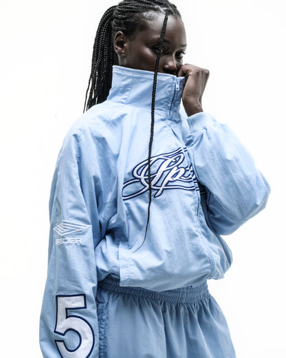 Light blue nylon track jacket with embroidered chest logo, sleeve graphic, and elastic cuffs.