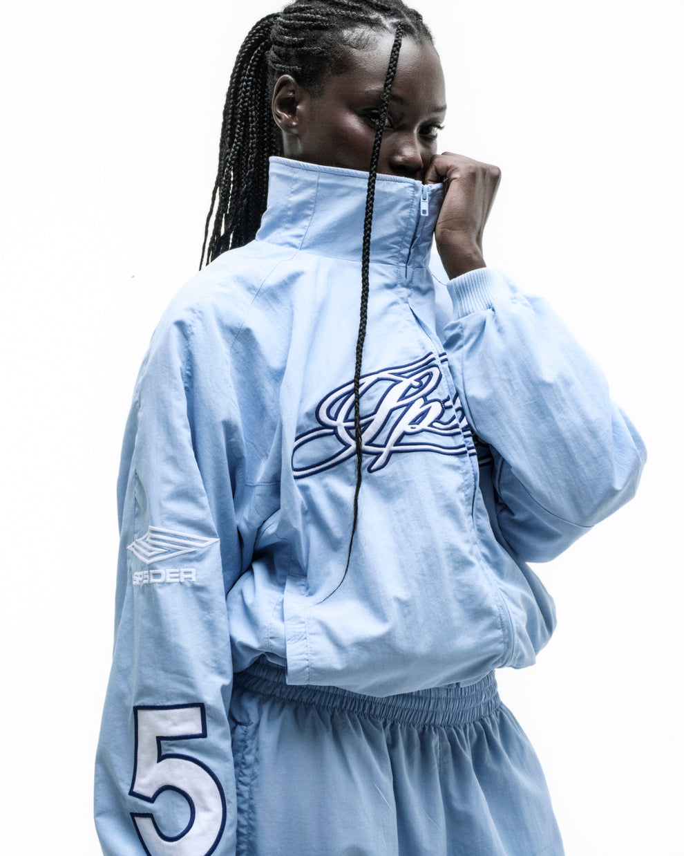 Light blue nylon track jacket with embroidered chest logo, sleeve graphic, and elastic cuffs.
