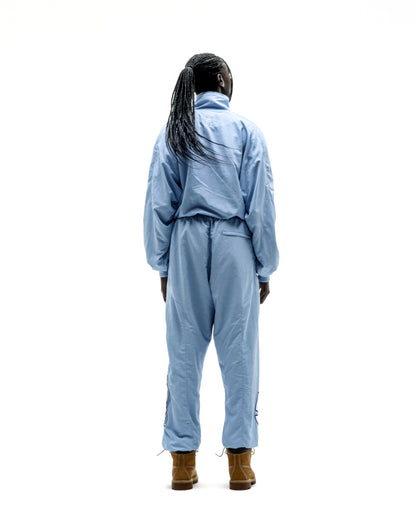 Person from behind wearing a light blue nylon track jacket and matching pants with brown boots.