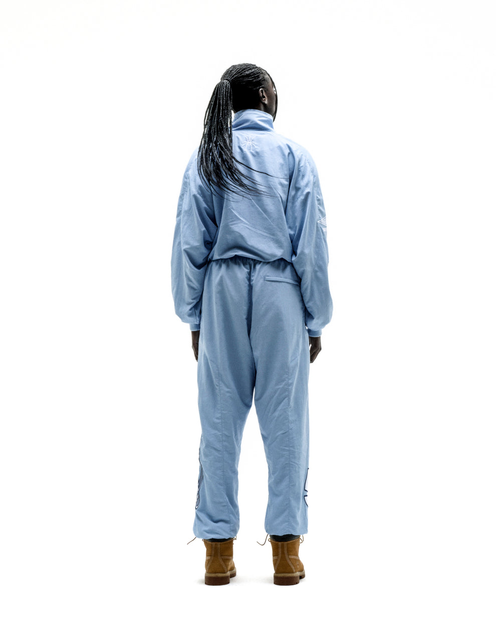 Person from behind wearing a light blue nylon track jacket and matching pants with brown boots.