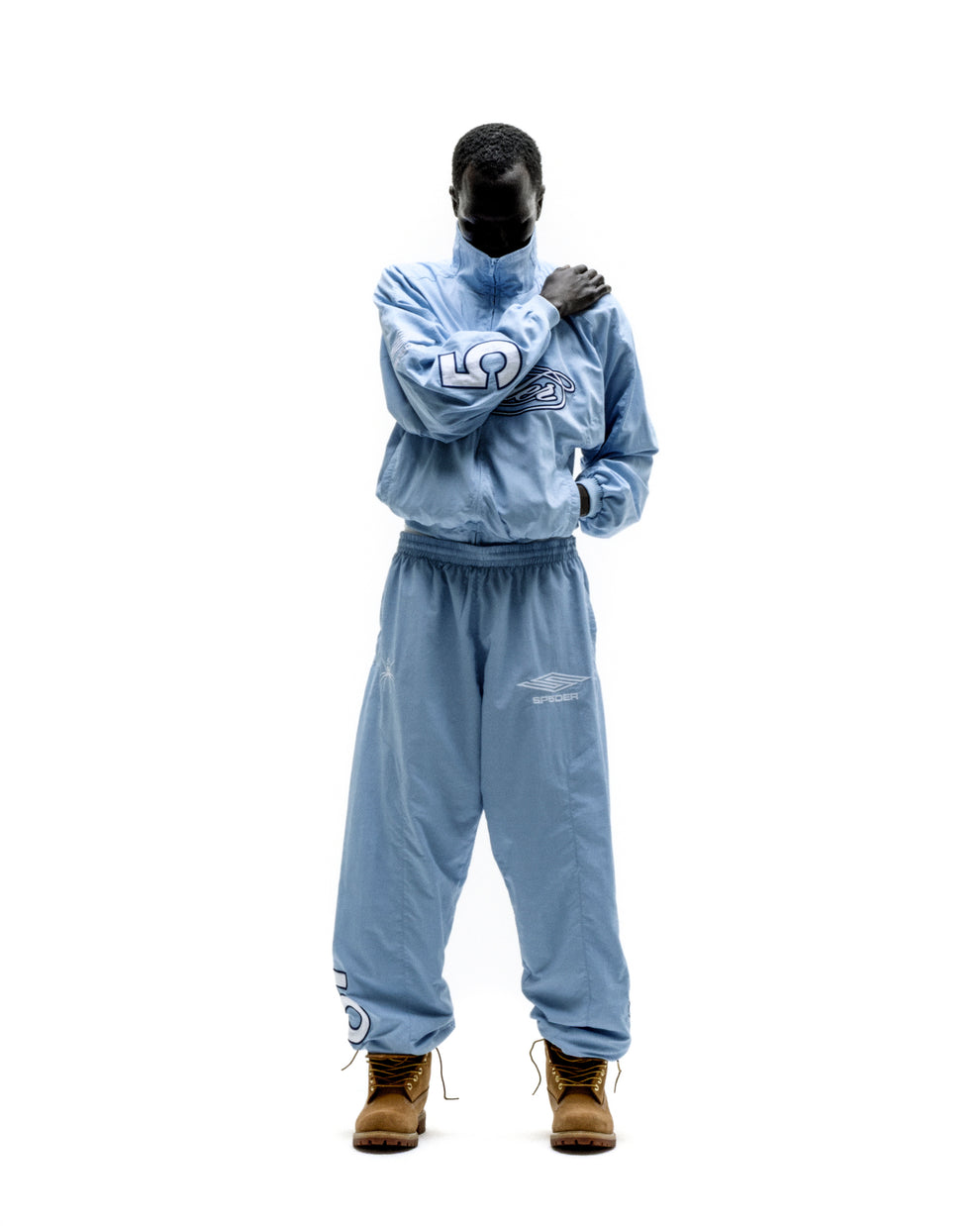 Light blue nylon track jacket with embroidered chest logo, full zip, stand collar, elastic cuffs, and matching pants.