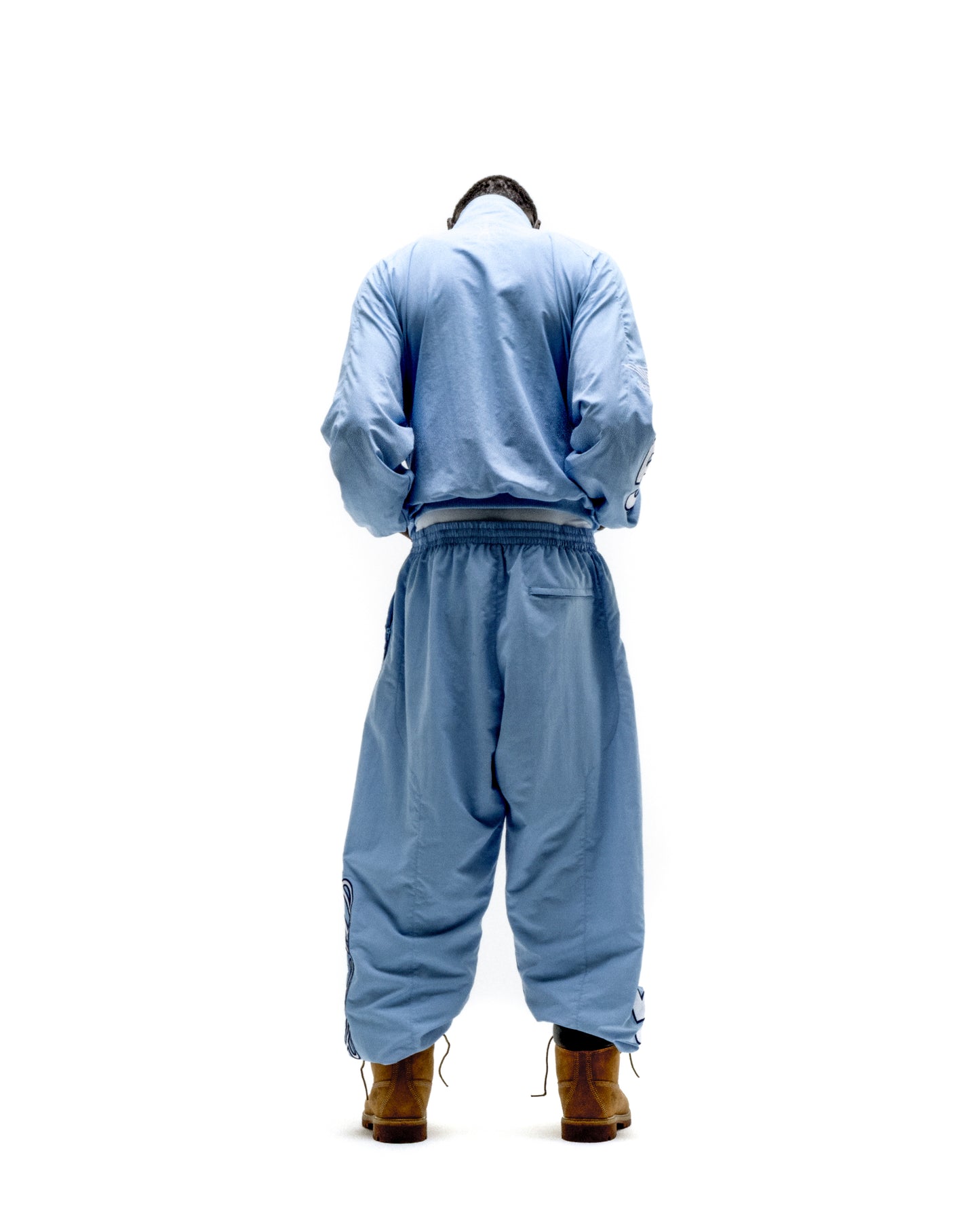 Light blue nylon track jacket and pants set with elastic cuffs and hem, worn with brown boots.