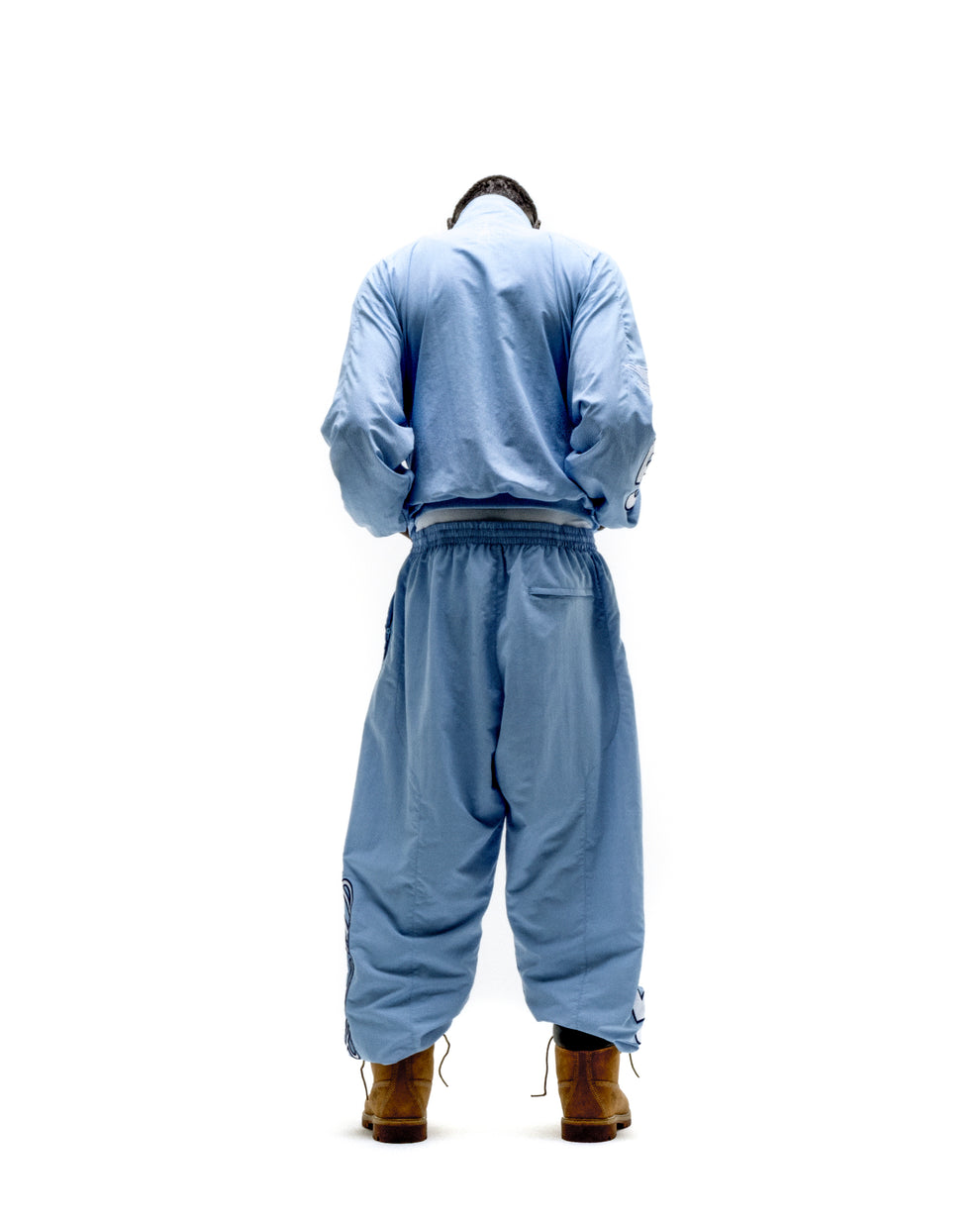 Light blue nylon track jacket and pants set with elastic cuffs and hem, worn with brown boots.