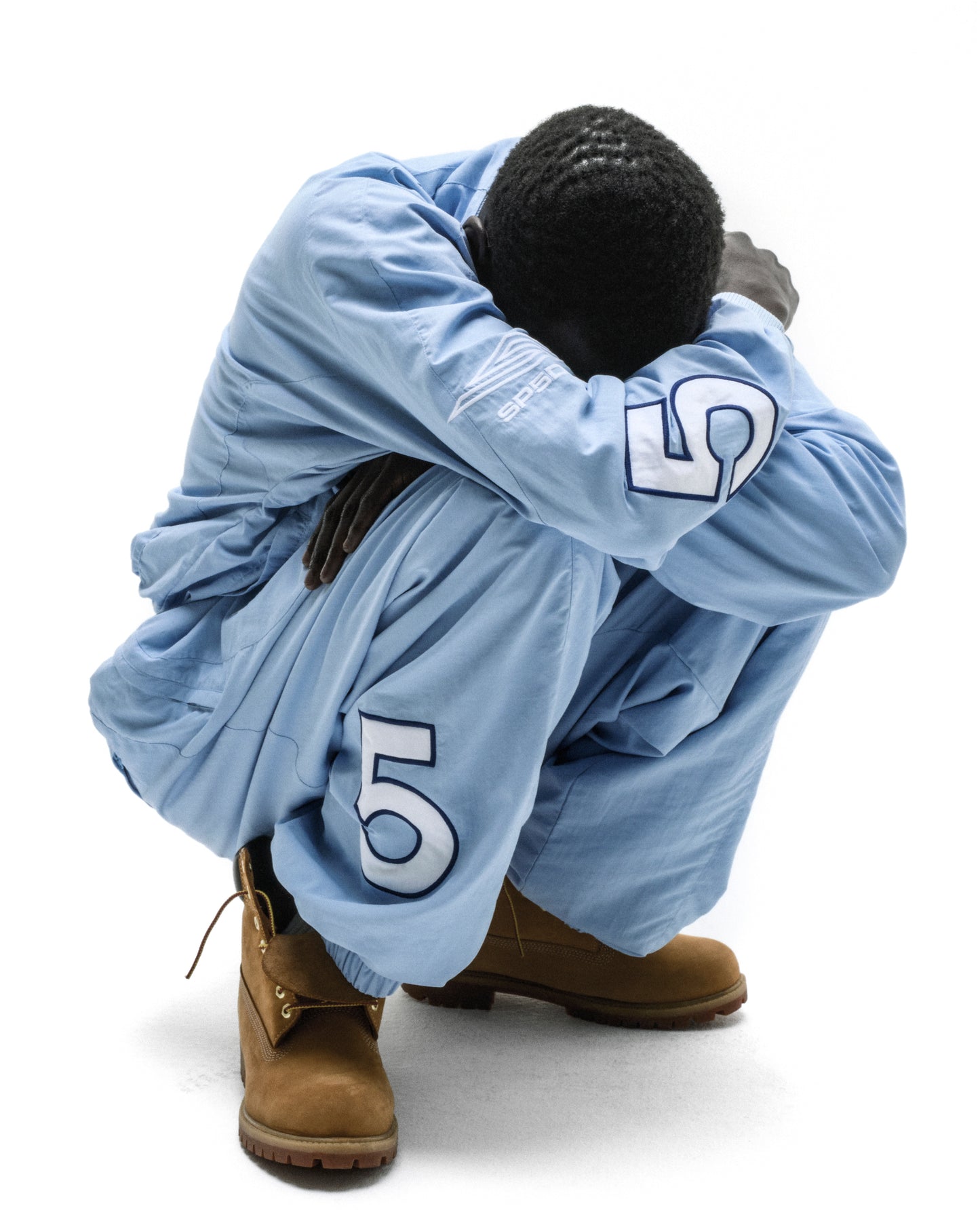 Man in light blue nylon track jacket and pants with "5" graphics, brown boots.