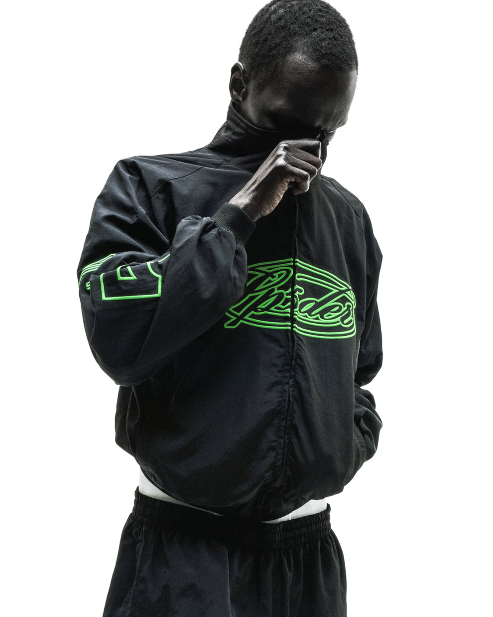 Black nylon track jacket with neon green embroidered chest logo and sleeve graphic.