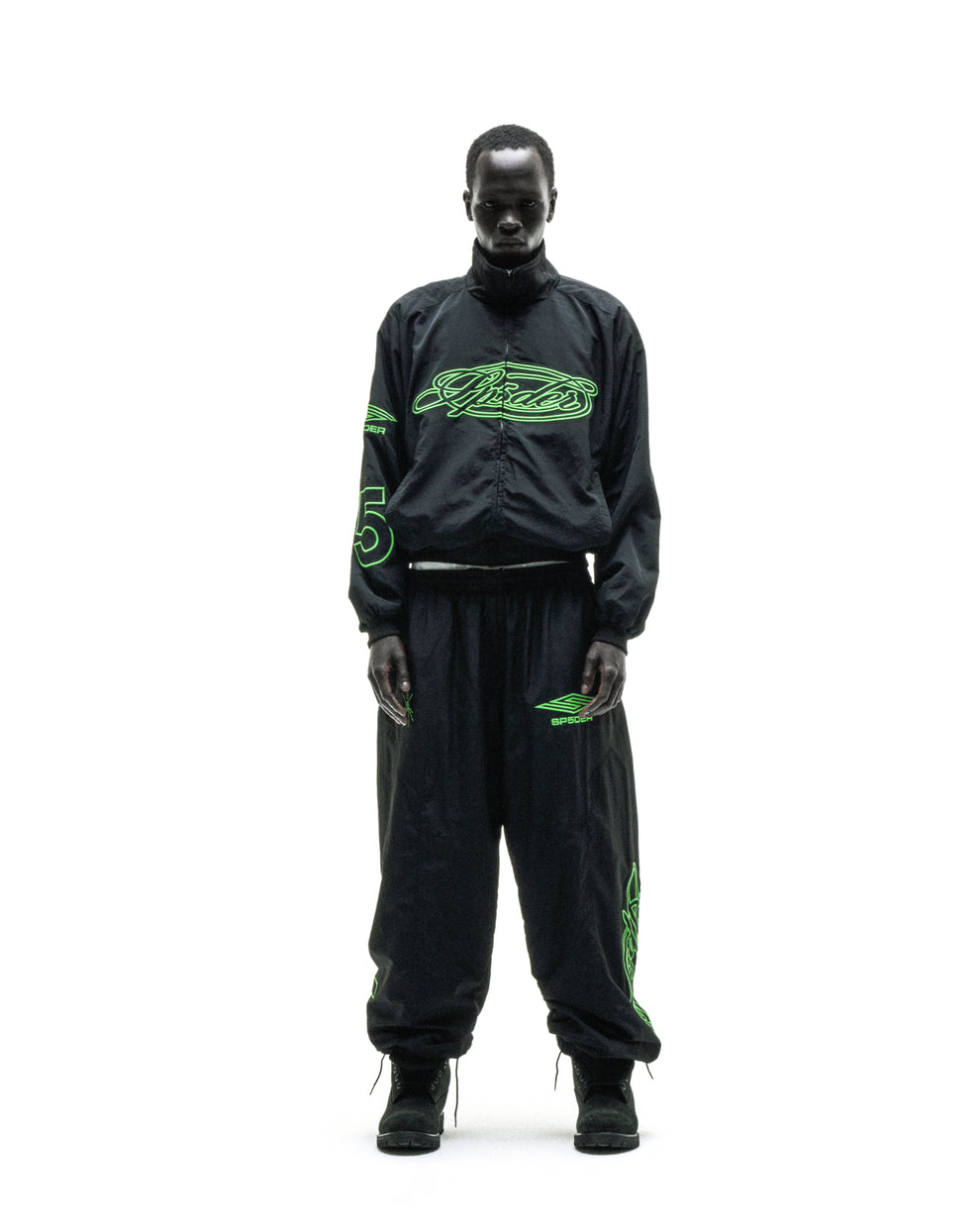 Black nylon track jacket with green embroidered chest logo, stand collar, and matching pants.