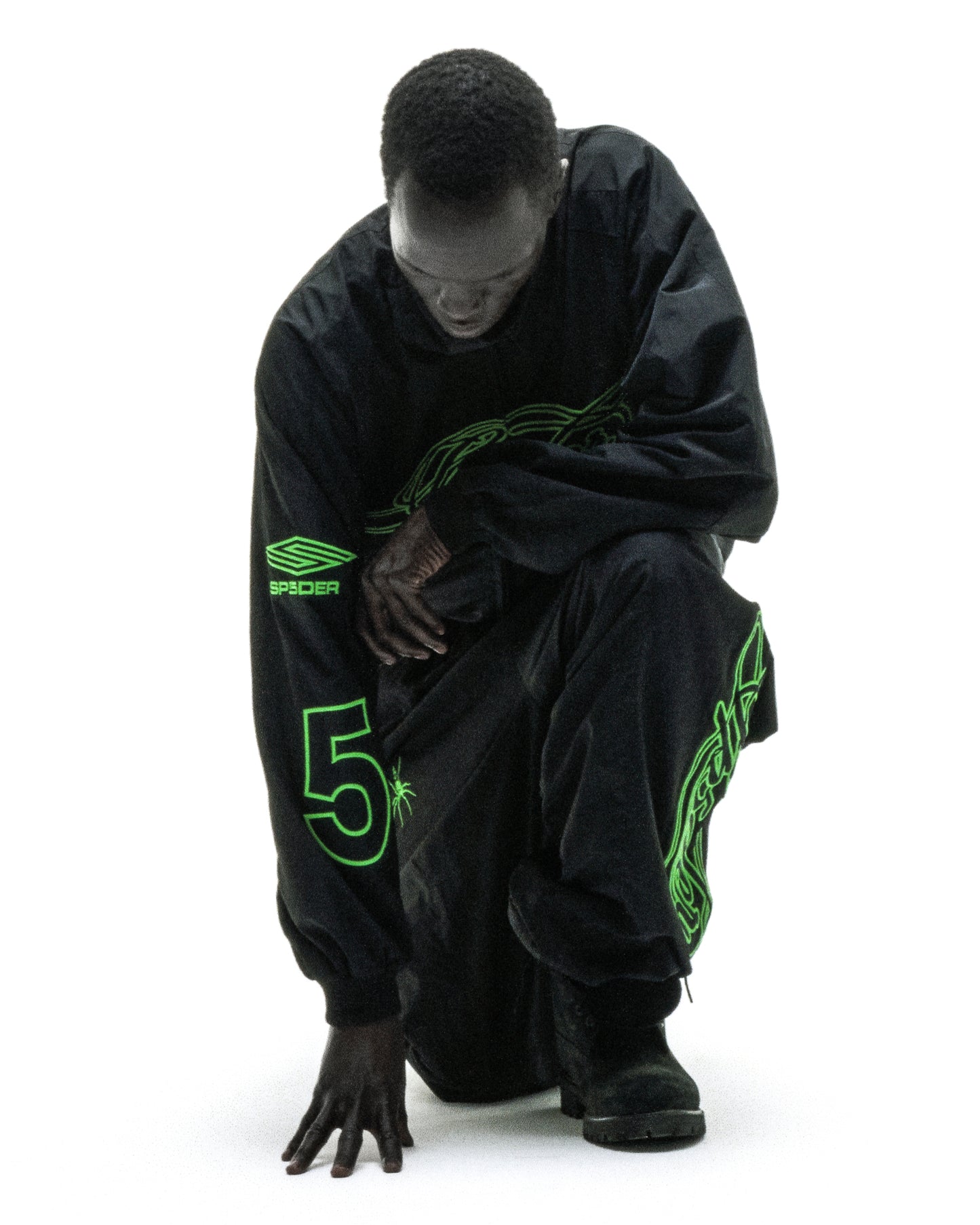 Black nylon track jacket with green embroidered chest logo, sleeve graphic, and "5" detail.