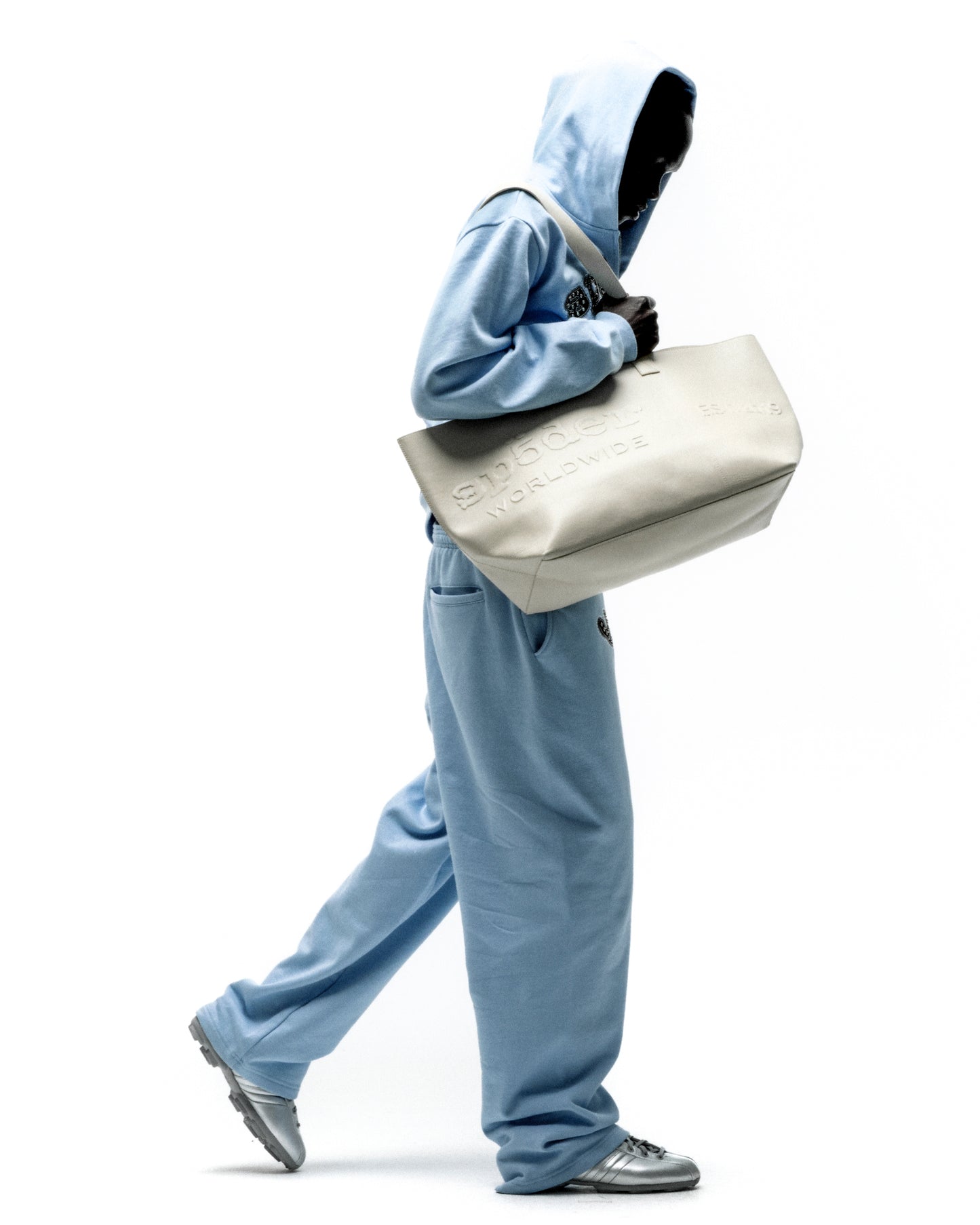 Structured genuine leather tote bag with embossed tonal logo, held by a person in a light blue tracksuit.