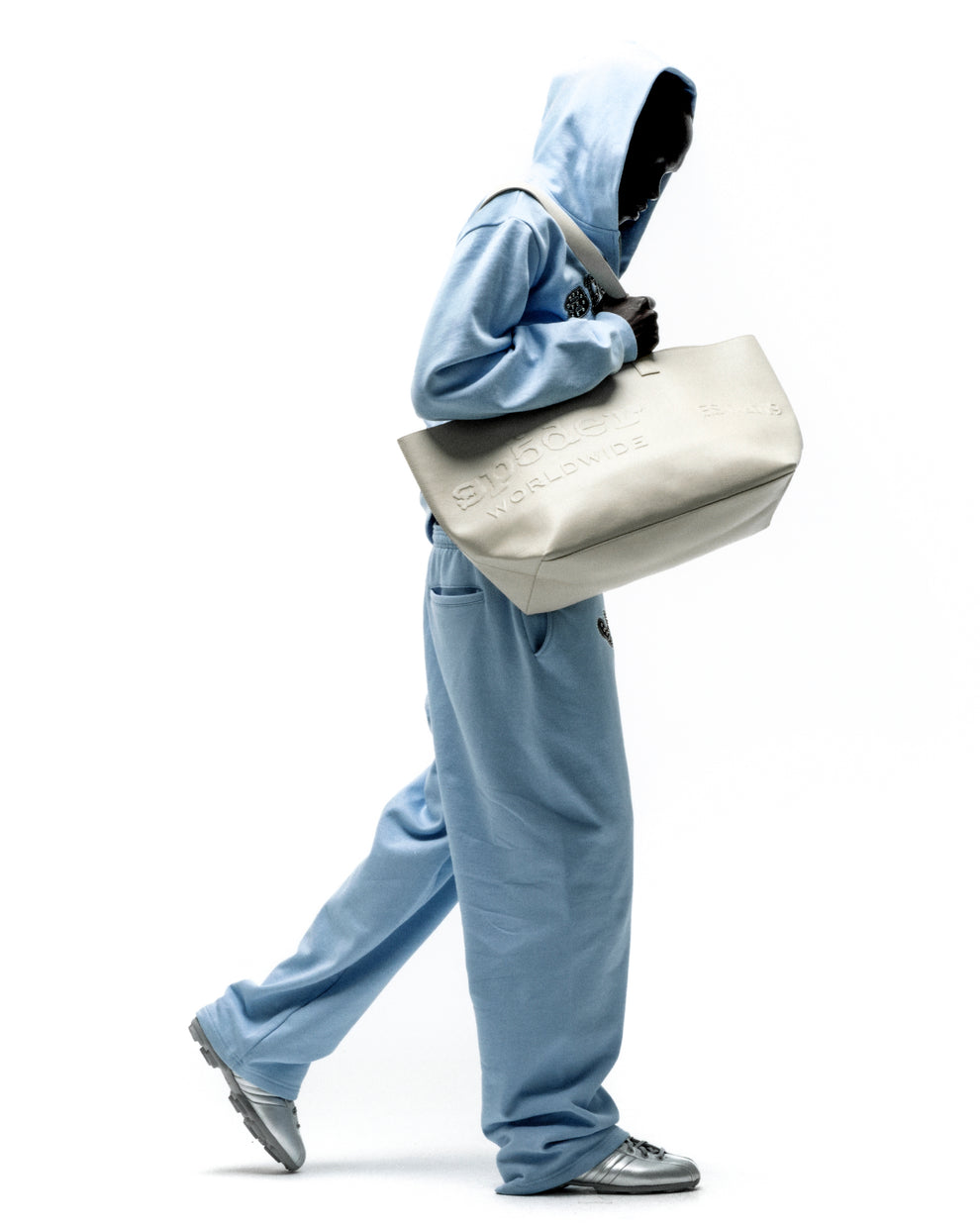 Structured genuine leather tote bag with embossed tonal logo, held by a person in a light blue tracksuit.