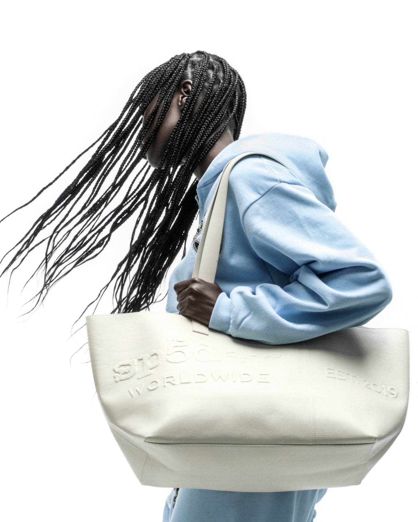 Cream leather tote bag with embossed "GHOST WORLDWIDE" and "EST. 2019" logos, held by a person.