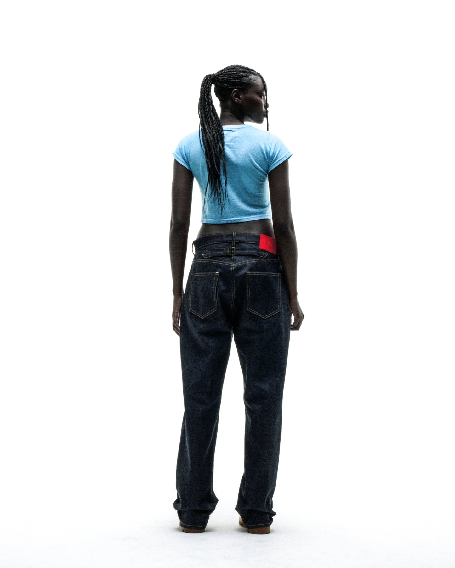 Dark-skinned model in a light blue cropped baby tee and dark wash baggy jeans, back to viewer.
