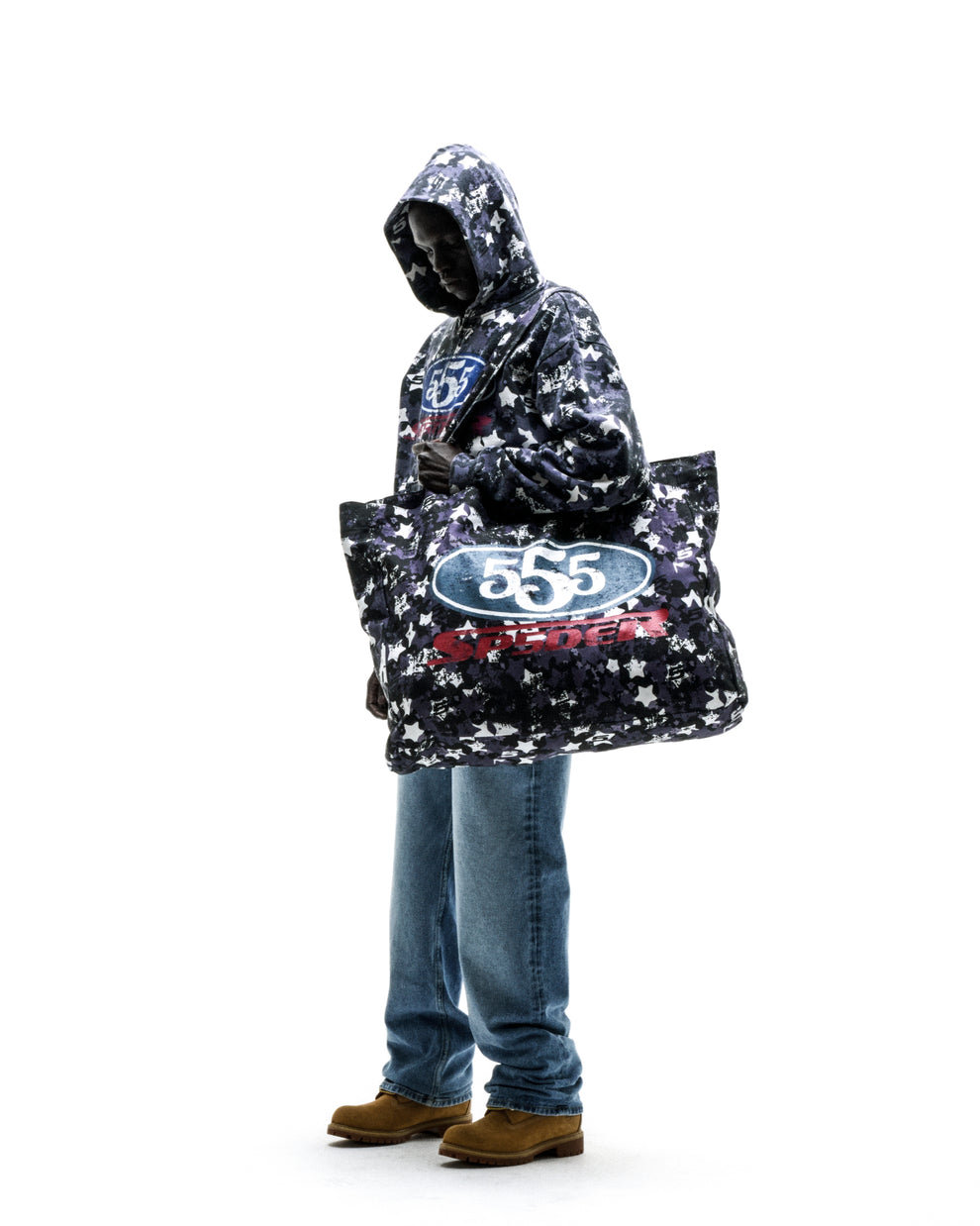 Model wearing a R5CING TOTE BAG, a large black and white star camo print twill bag with "555" graphic.