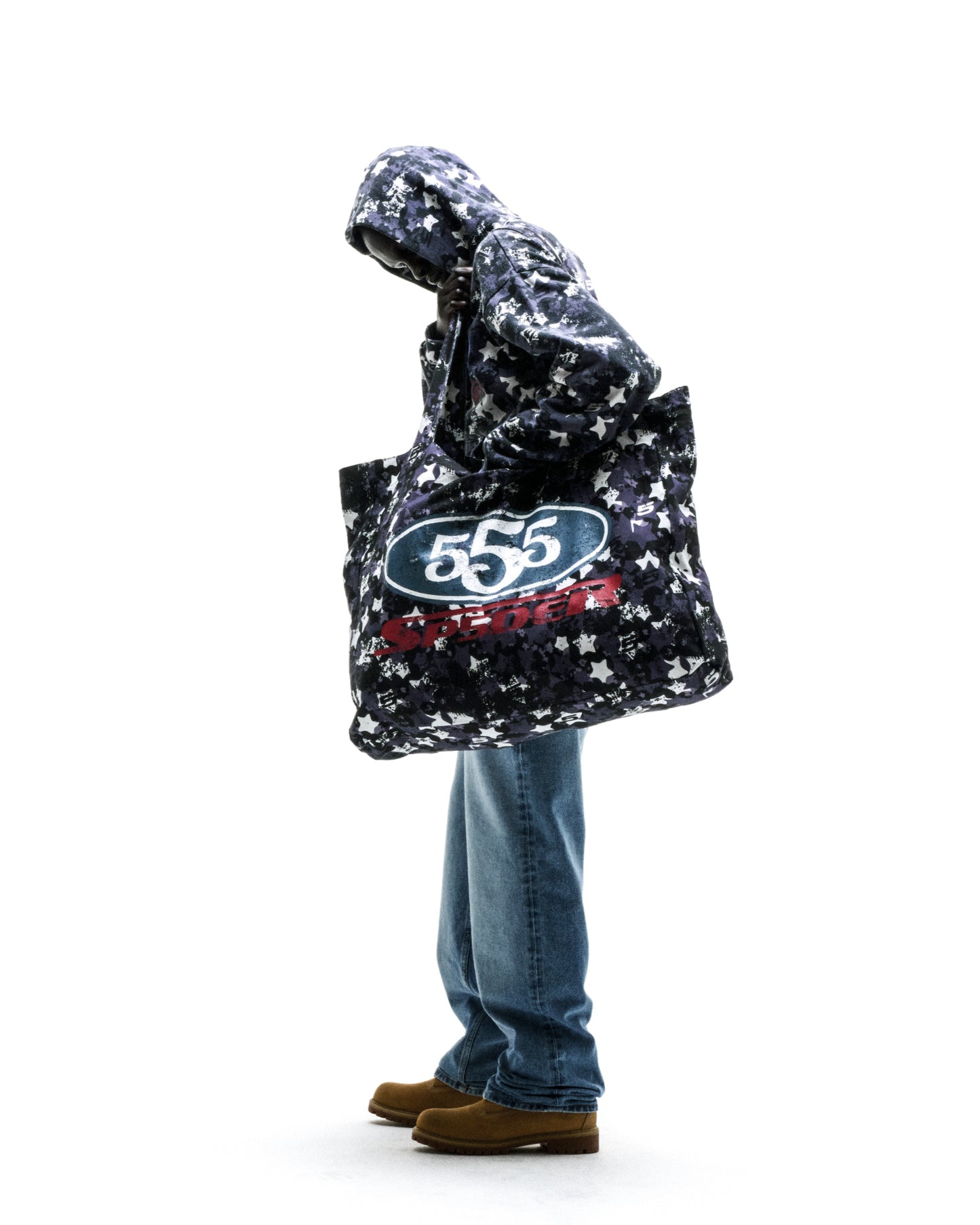R5CING TOTE BAG: Brushed twill tote with star camo print and "555" graphic, held by person in jeans.