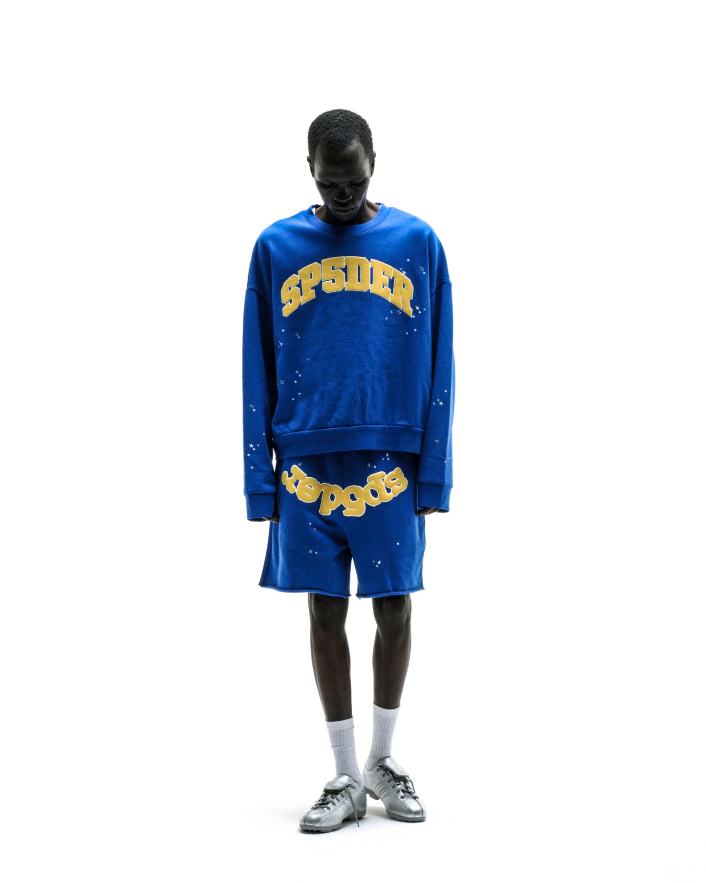 Blue varsity crewneck sweatshirt with yellow "SP5DER" lettering and graphic print on front.