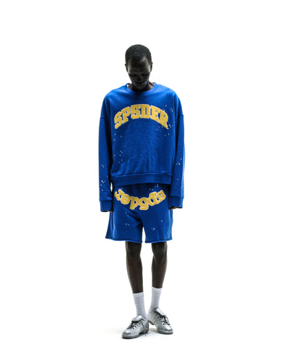 Blue varsity crewneck sweatshirt with yellow "SP5DER" lettering and graphic print on front.