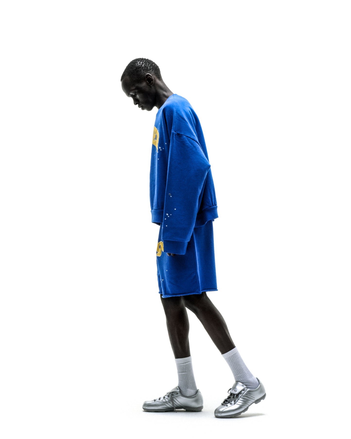 Blue oversized crewneck sweatshirt with long sleeves and yellow graphic on left sleeve, paired with matching blue shorts.