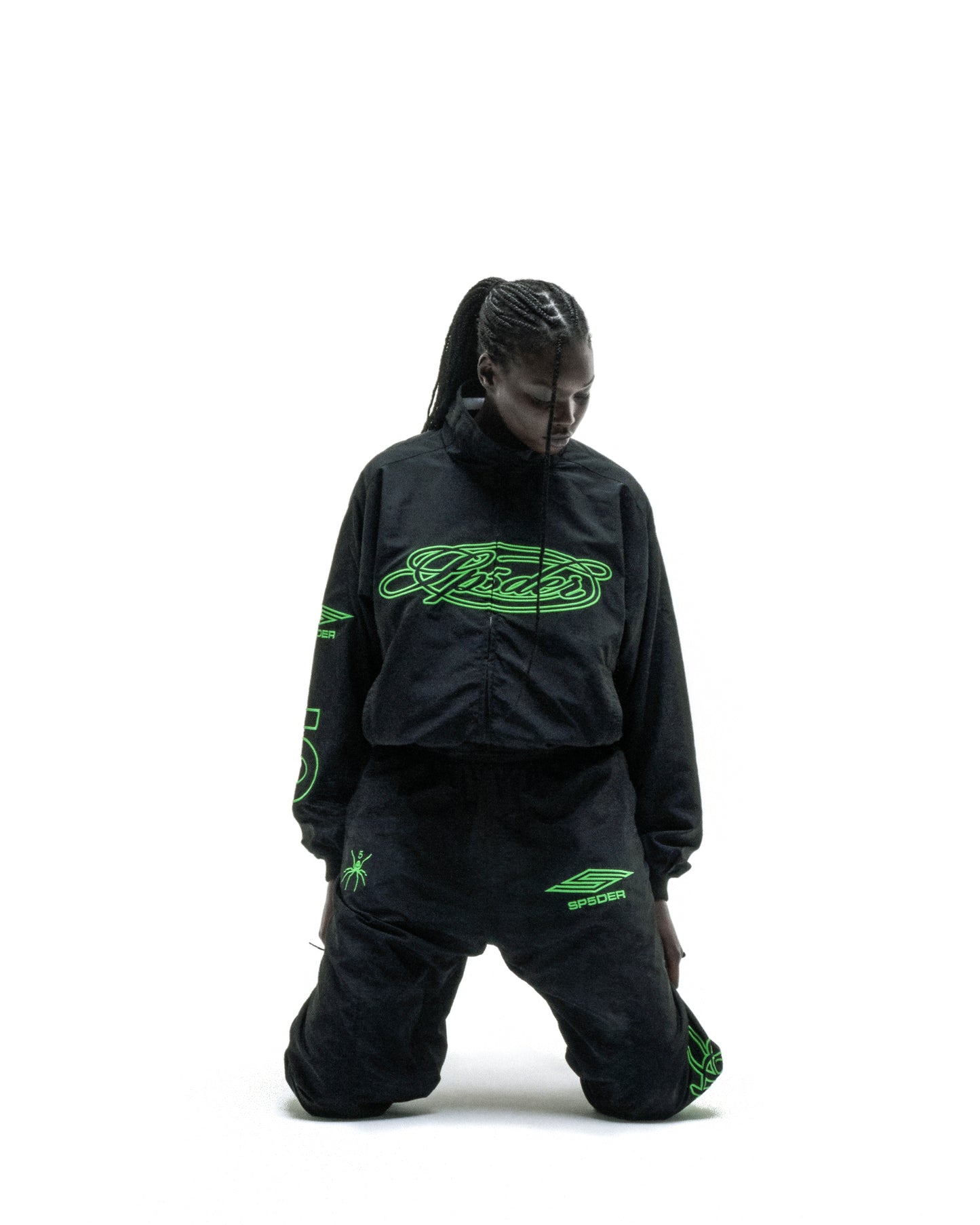 Black nylon track jacket with green embroidered chest logo, matching pants, and sleeve graphic.