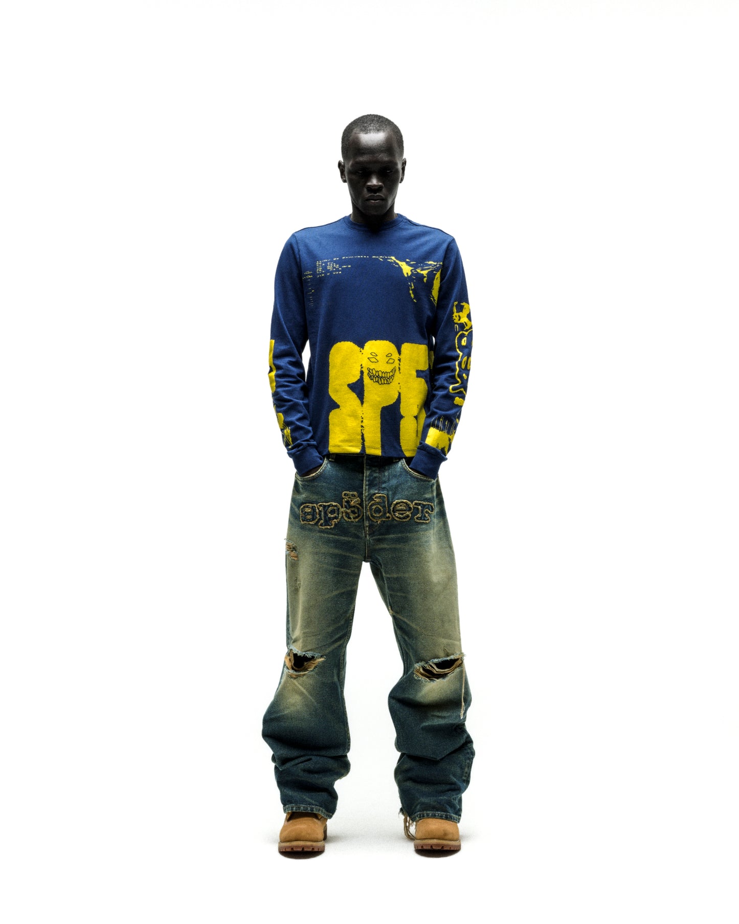 Model in blue X-RAY LONGSLEEVE with yellow graphic print on front, back, and sleeves, paired with distressed jeans.