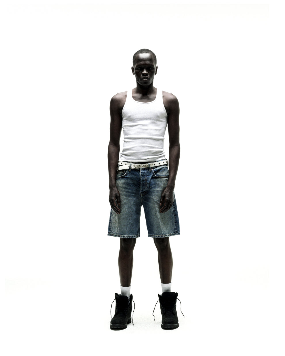 Man wearing vintage wash denim shorts with rhinestone web design, a white tank top, and black boots.