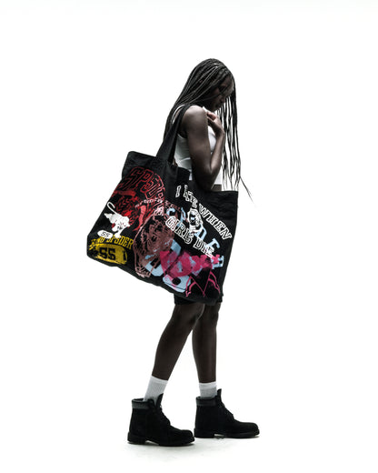 Black 8oz twill tote bag with vibrant multi-color graphic print, carried by a person.