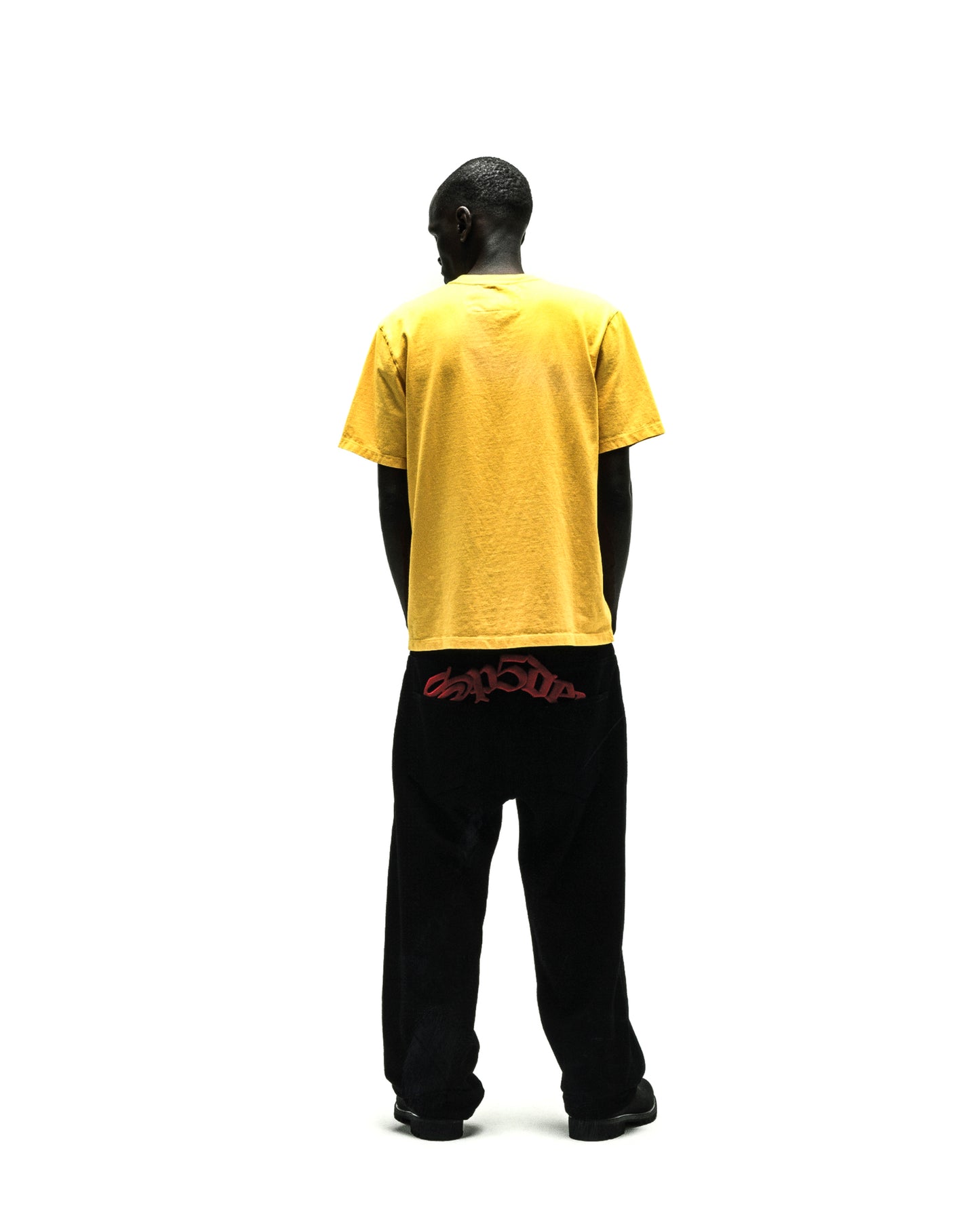 Rear view of a person wearing a yellow cotton tee and black pants with red text.