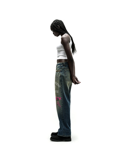 Woman in faded blue BIG PRINT JEANS with pink and white graphic designs, white tank top, and black boots.