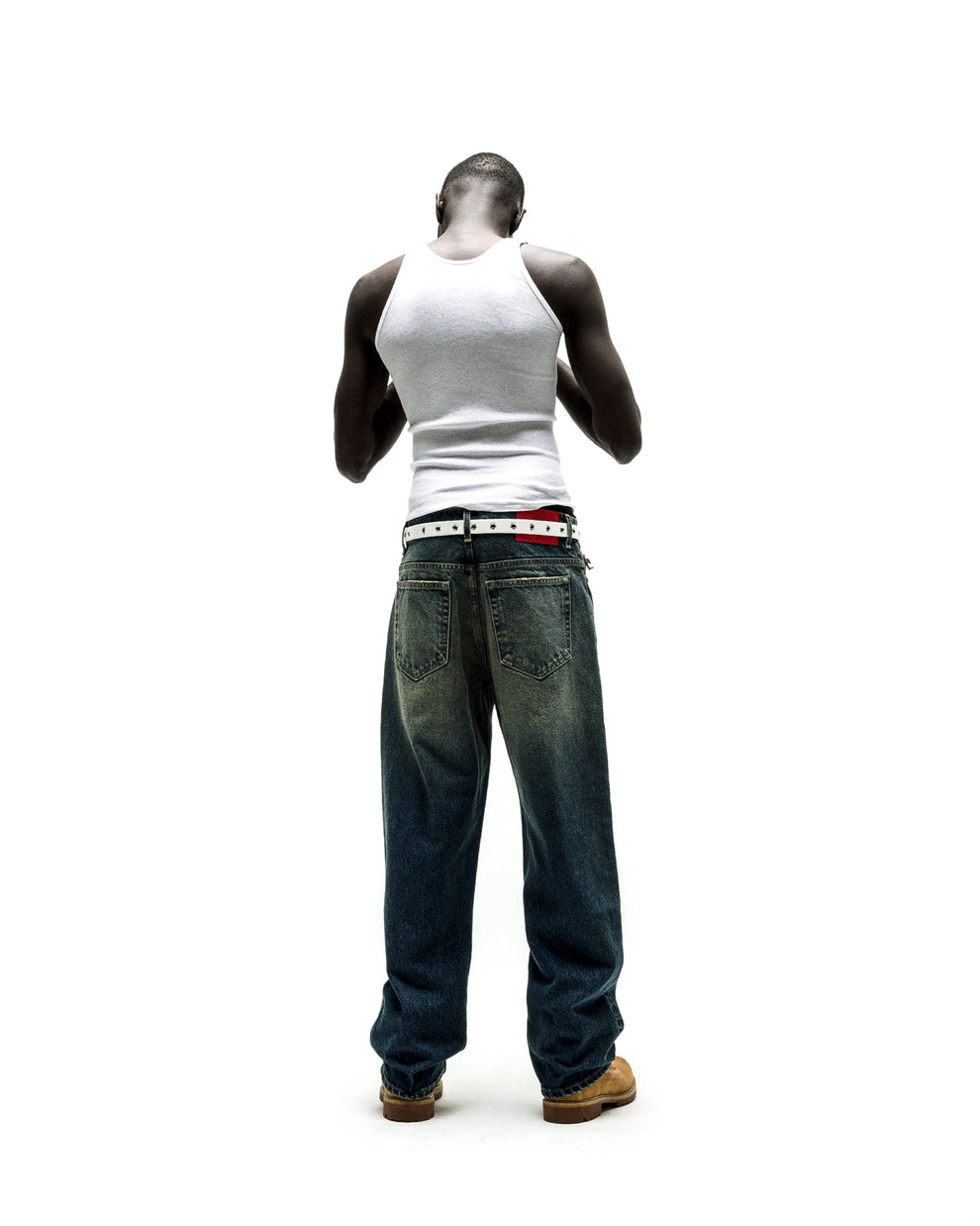 Man from behind wearing baggy, dark wash BIG PRINT JEANS with a white belt and tank top.
