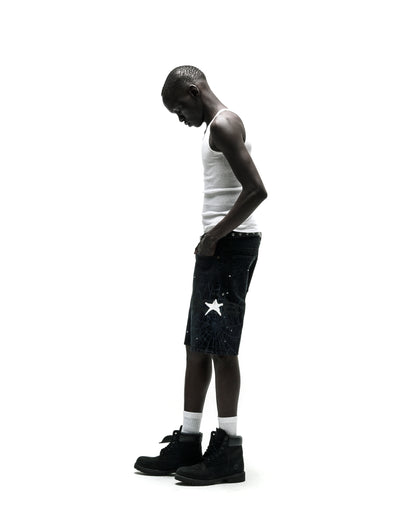 Man in dark wash HEAVY WEB JEAN SHORTS with white star graphic, white tank top, and black boots.
