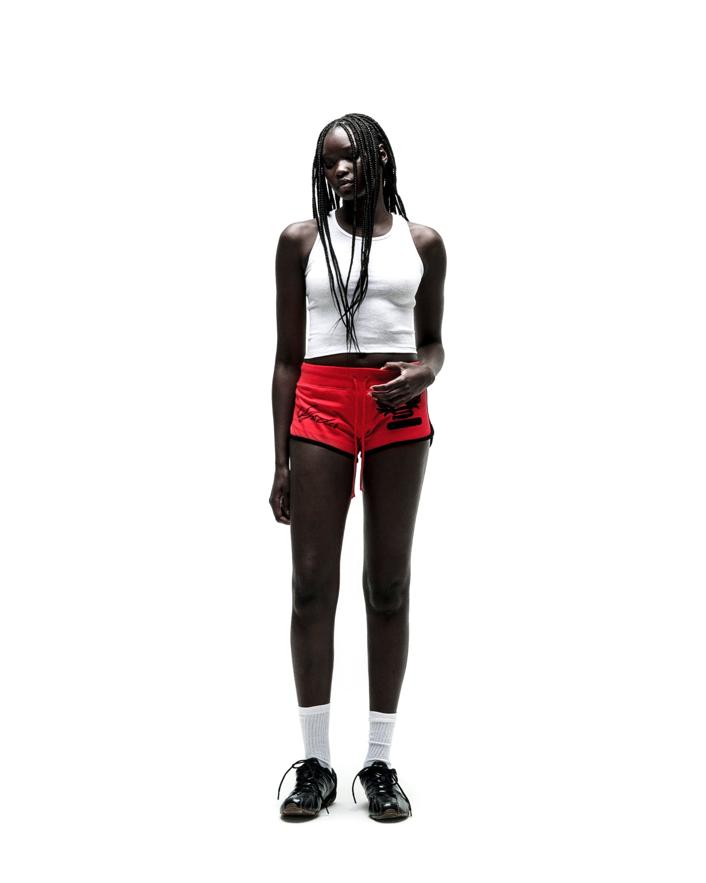 Woman in red SP5 WIDE BOXER shorts with black trim, white crop top, and black sneakers.